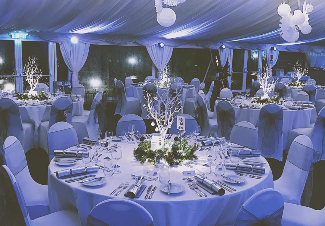 a table in a marquee with chairs set with white festive decorations